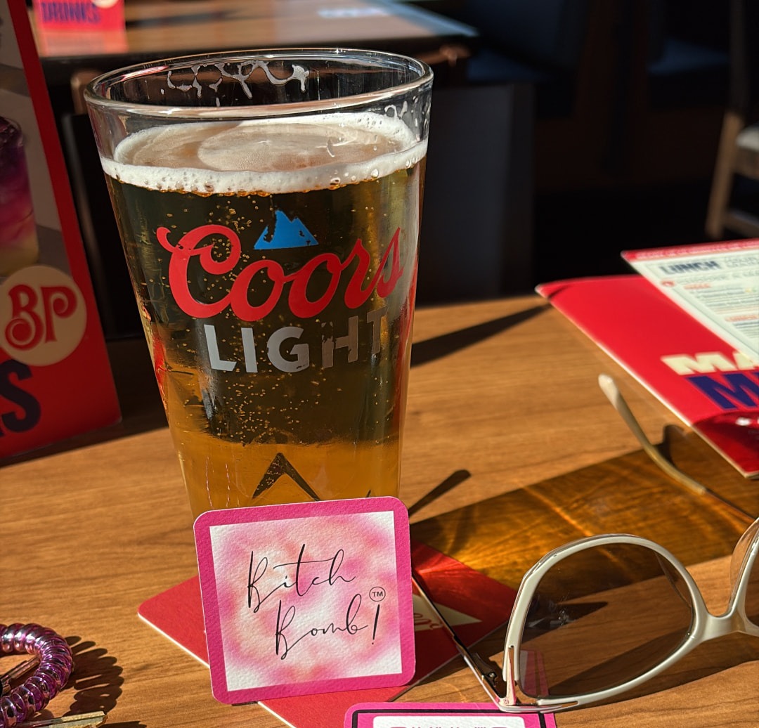 A Bitch Bomb!™ card dropped beside a beer on a sunny patio table
